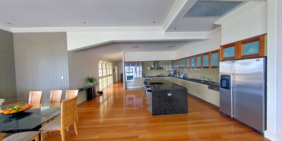 Offene, Große Moderne Küche in L-Form mit Doppelwaschbecken, Glasfronten, hellbraunen Holzschränken, Granit-Arbeitsplatte, Glasrückwand, Küchengeräten aus Edelstahl, braunem Holzboden, Kücheninsel, eingelassener Decke, Küchenrückwand in Grau und grauer Arbeitsplatte in Brisbane