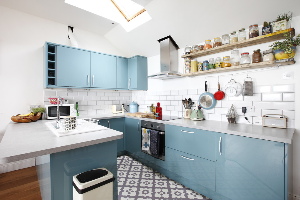Bild på ett litet nordiskt kök, med en nedsänkt diskho, släta luckor, blå skåp, laminatbänkskiva, vitt stänkskydd, stänkskydd i tunnelbanekakel, svarta vitvaror, klinkergolv i keramik och en halv köksö