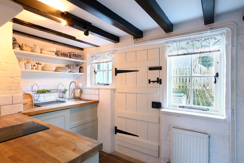Bild på ett avskilt, litet lantligt l-kök, med en rustik diskho, släta luckor, grå skåp, träbänkskiva, vitt stänkskydd, stänkskydd i tunnelbanekakel, integrerade vitvaror och tegelgolv