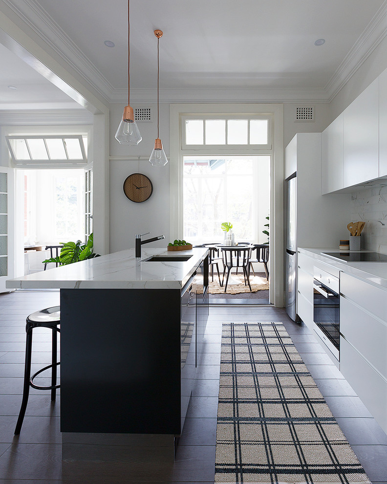 Foto på ett minimalistiskt kök, med en undermonterad diskho, vita skåp, vitt stänkskydd och en köksö