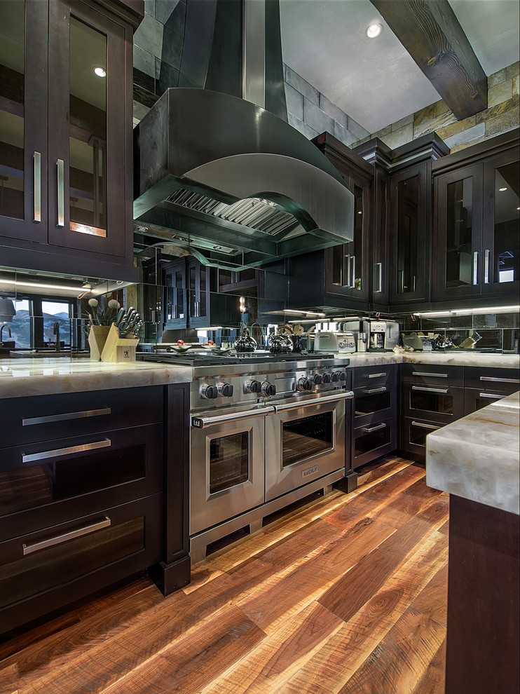 Klassische Wohnküche mit Glasfronten, dunklen Holzschränken, Quarzit-Arbeitsplatte, Küchengeräten aus Edelstahl, Kücheninsel, Rückwand aus Spiegelfliesen und braunem Holzboden in Denver
