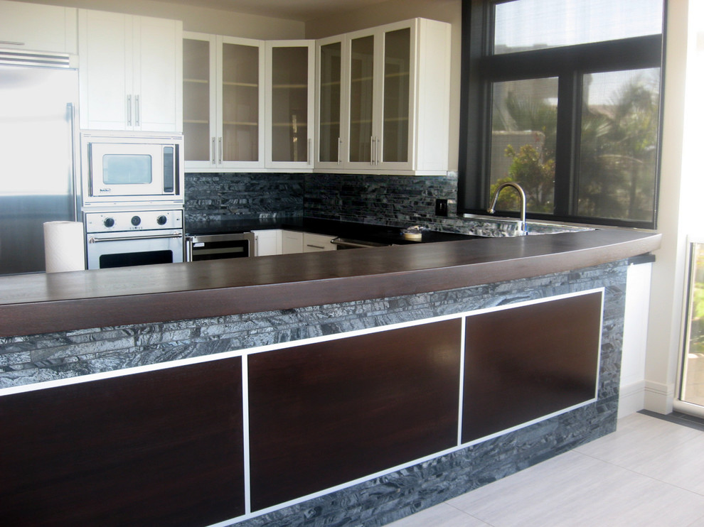 Photo of a medium sized contemporary u-shaped kitchen/diner in San Diego with a submerged sink, shaker cabinets, white cabinets, grey splashback, stone tiled splashback, stainless steel appliances, light hardwood flooring and no island.