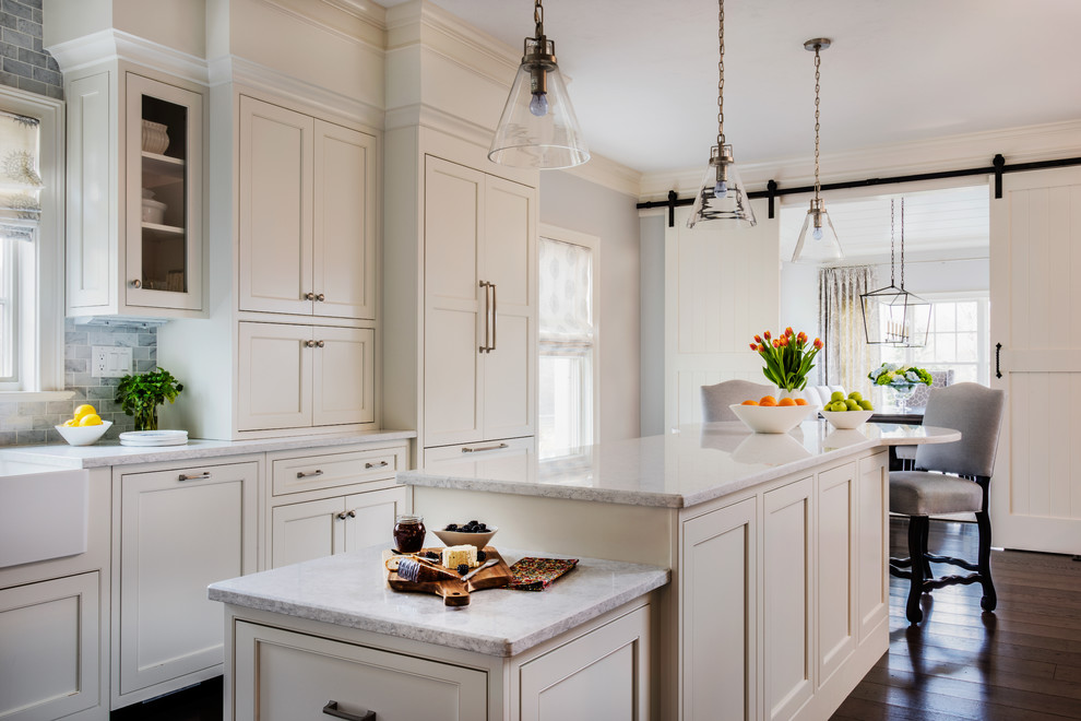 This is an example of a traditional kitchen in Boston with a belfast sink, beaded cabinets, white cabinets, grey splashback, dark hardwood flooring, an island and brown floors.