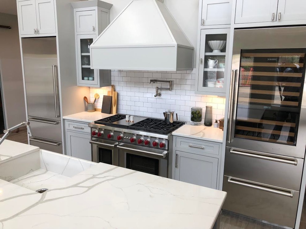 Idéer för att renovera ett mellanstort lantligt vit vitt kök, med en integrerad diskho, luckor med infälld panel, grå skåp, bänkskiva i kvartsit, vitt stänkskydd, stänkskydd i tunnelbanekakel, rostfria vitvaror och en köksö