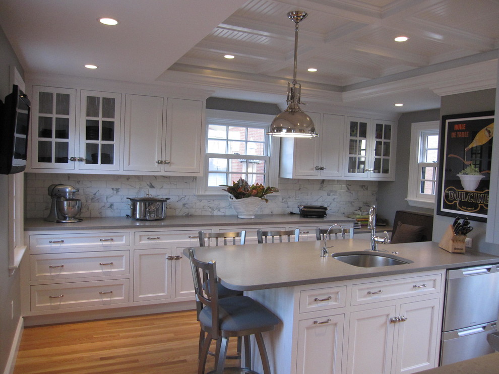 Inredning av ett klassiskt stort grå grått kök, med en undermonterad diskho, skåp i shakerstil, vita skåp, bänkskiva i kvarts, vitt stänkskydd, stänkskydd i marmor, rostfria vitvaror, mellanmörkt trägolv och en halv köksö