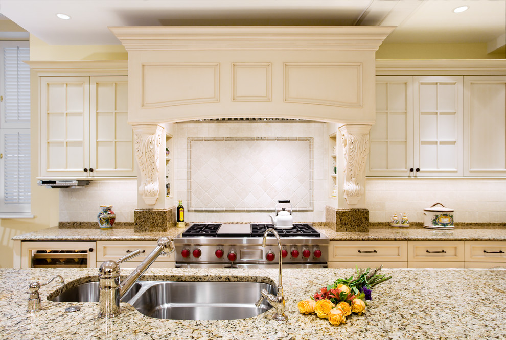 Exempel på ett mellanstort klassiskt beige beige kök, med en undermonterad diskho, luckor med infälld panel, vita skåp, granitbänkskiva, beige stänkskydd, stänkskydd i travertin, rostfria vitvaror, ljust trägolv och en köksö