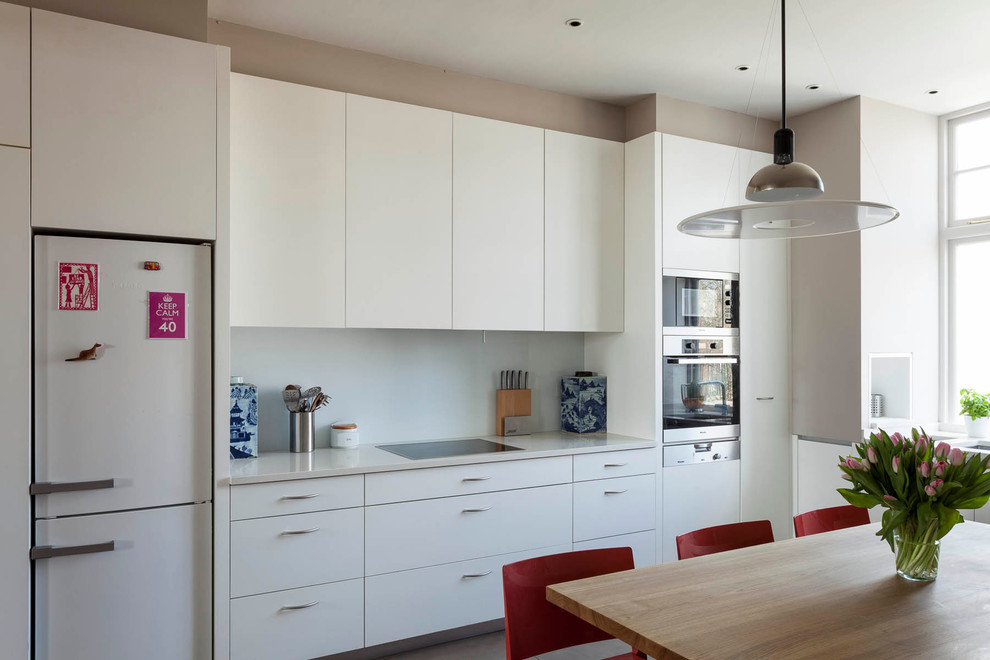 This is an example of a contemporary l-shaped kitchen/diner in London with flat-panel cabinets, white cabinets, white splashback and white appliances.