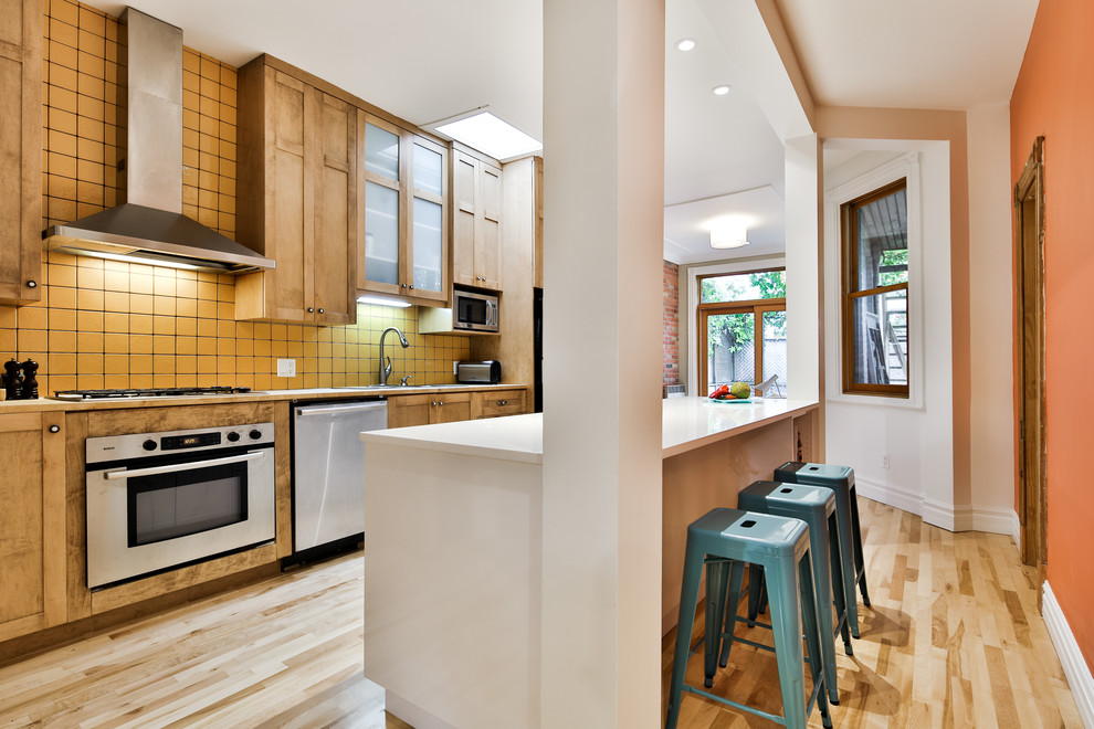 На фото: параллельная кухня среднего размера в современном стиле с кладовкой, плоскими фасадами, желтыми фасадами, стеклянной столешницей, фартуком из цементной плитки, светлым паркетным полом и островом