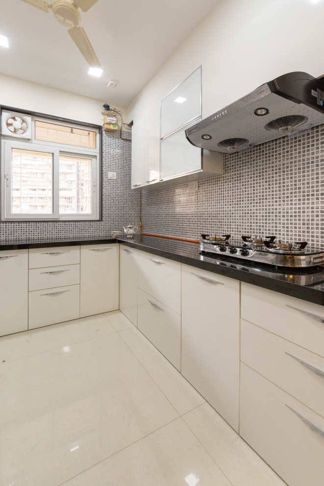 Mittelgroße Moderne Küche ohne Insel in L-Form mit flächenbündigen Schrankfronten, beigen Schränken, Küchenrückwand in Grau, beigem Boden und schwarzer Arbeitsplatte in Pune