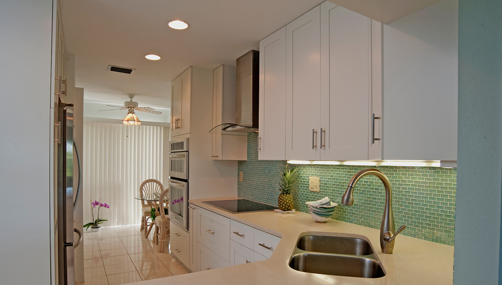 Medium sized traditional l-shaped enclosed kitchen in Chicago with a double-bowl sink, raised-panel cabinets, white cabinets, engineered stone countertops, blue splashback, glass tiled splashback, stainless steel appliances, porcelain flooring, an island and white floors.