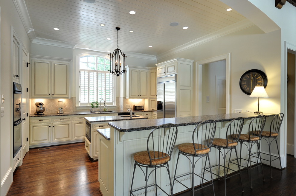 Inspiration for a large timeless u-shaped laminate floor and brown floor enclosed kitchen remodel in Atlanta with an undermount sink, raised-panel cabinets, white cabinets, granite countertops, beige backsplash, stone tile backsplash, stainless steel appliances and an island