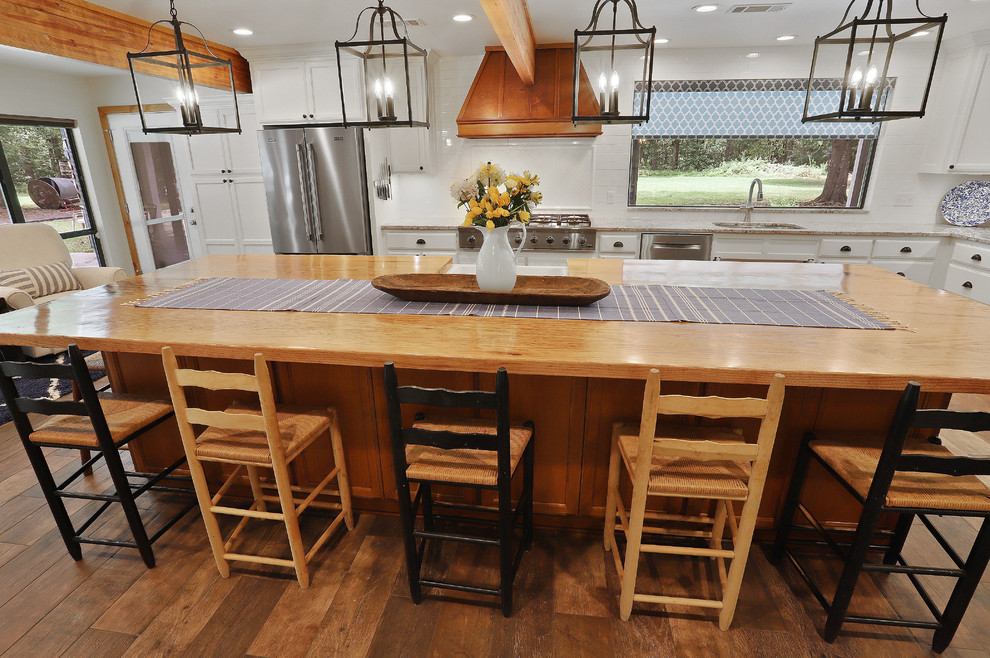 This is an example of a large rustic u-shaped open plan kitchen in New Orleans with a belfast sink, white cabinets, wood worktops, white splashback, metro tiled splashback, stainless steel appliances, porcelain flooring, an island, brown floors, multicoloured worktops and raised-panel cabinets.
