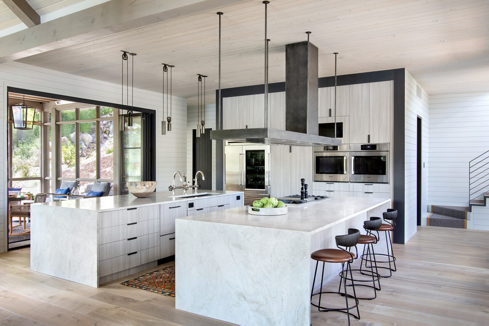 Rustic u-shaped kitchen in Other with a submerged sink, flat-panel cabinets, grey cabinets, stainless steel appliances, medium hardwood flooring, multiple islands, brown floors and grey worktops.