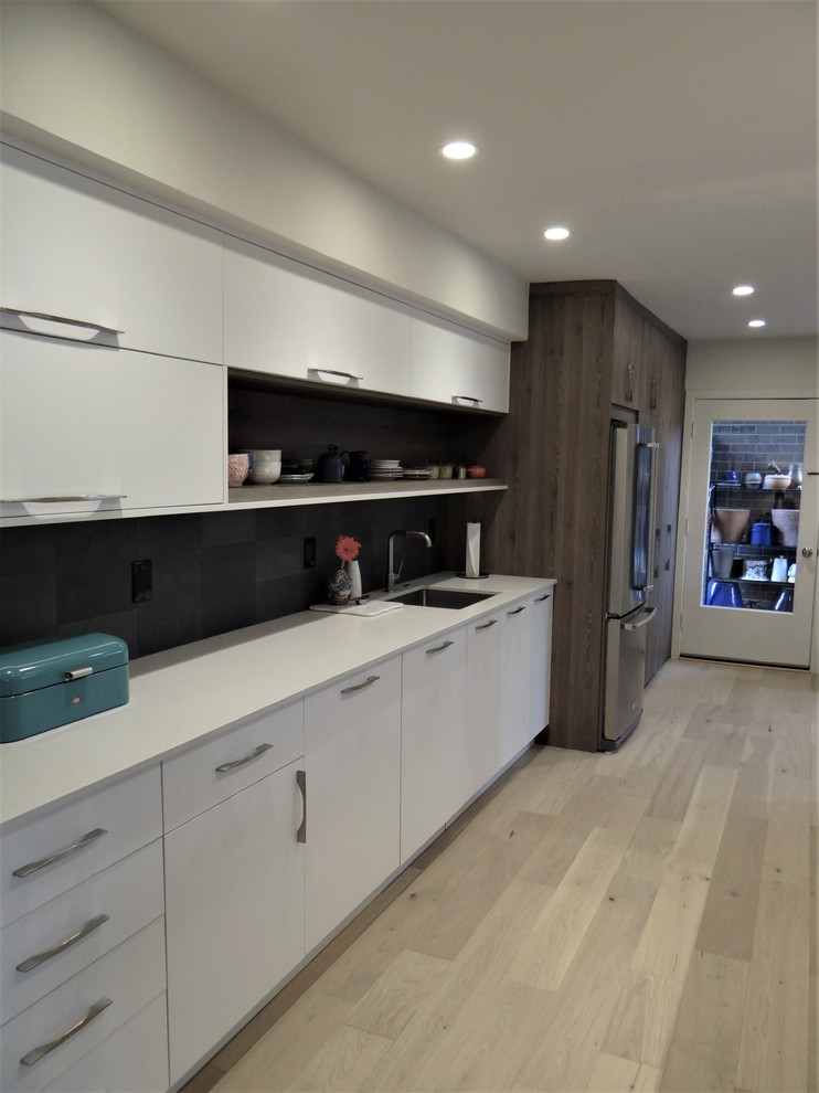 Photo of a medium sized modern galley kitchen/diner in DC Metro with a submerged sink, flat-panel cabinets, white cabinets, engineered stone countertops, grey splashback, stone tiled splashback, stainless steel appliances, light hardwood flooring, no island, brown floors and grey worktops.