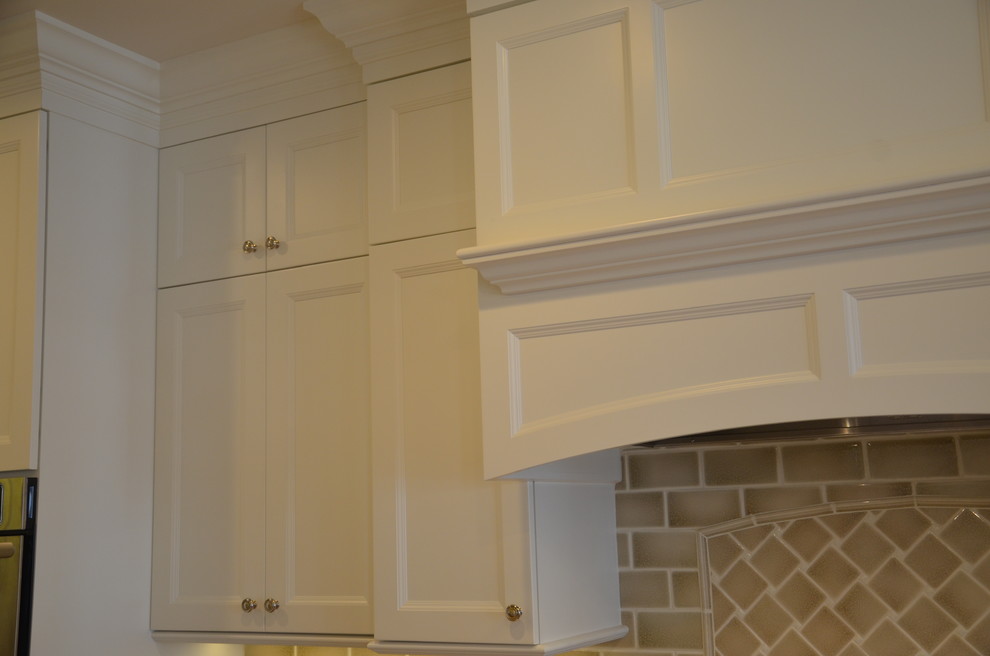 Example of a large classic l-shaped medium tone wood floor enclosed kitchen design in DC Metro with an undermount sink, recessed-panel cabinets, white cabinets, granite countertops, beige backsplash, ceramic backsplash, stainless steel appliances and a peninsula