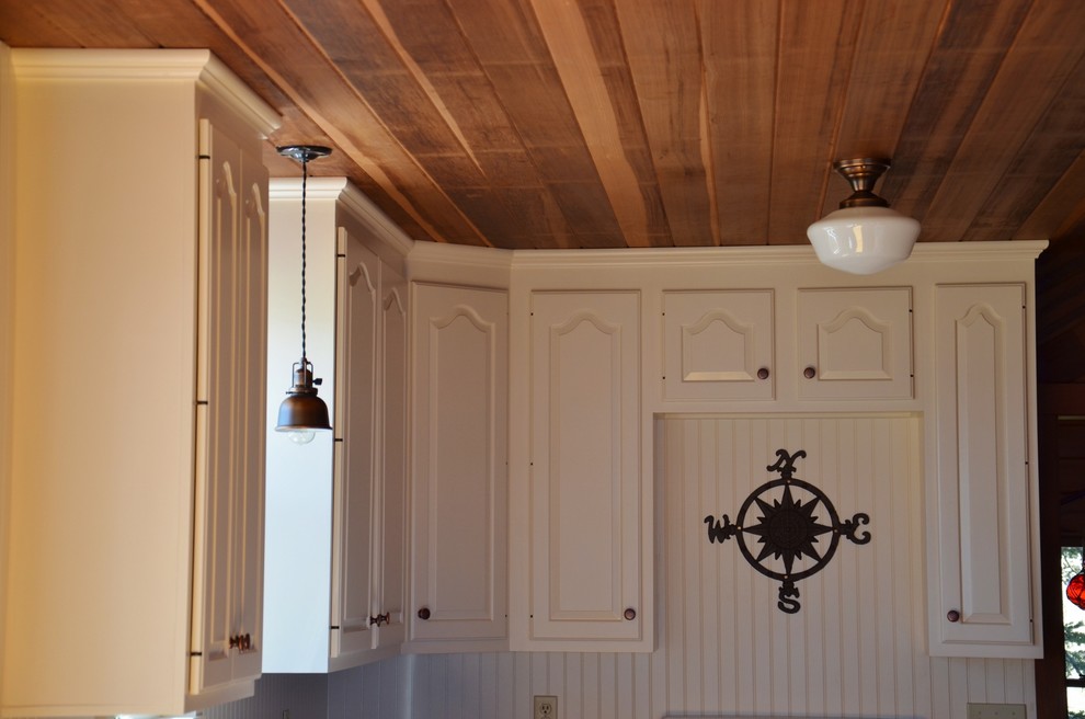 Photo of a small beach style l-shaped kitchen/diner in Portland Maine with raised-panel cabinets and white cabinets.