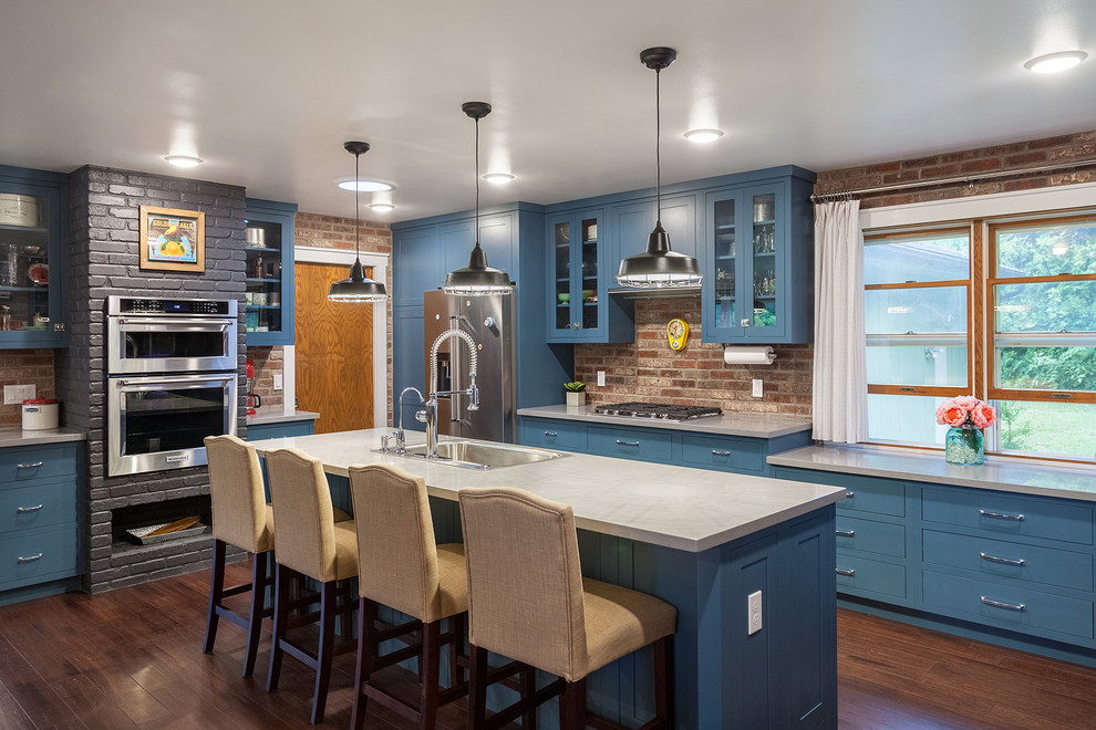 Geschlossene Klassische Küche mit blauen Schränken, Mineralwerkstoff-Arbeitsplatte, Rückwand aus Backstein, Küchengeräten aus Edelstahl, dunklem Holzboden, Kücheninsel, braunem Boden, Waschbecken und flächenbündigen Schrankfronten in Sonstige