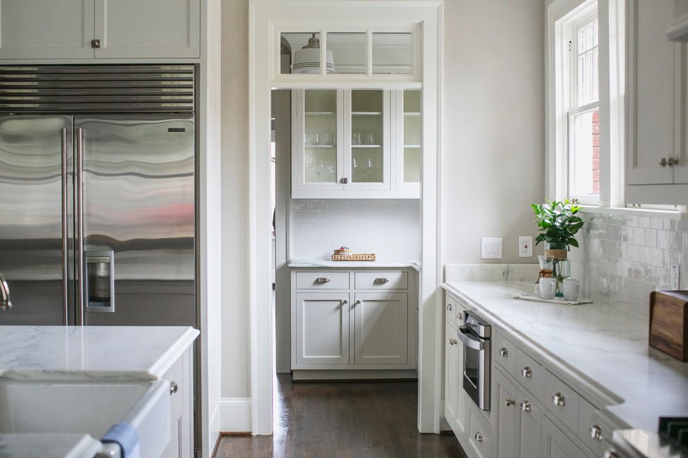 Amerikansk inredning av ett kök med öppen planlösning, med en rustik diskho, vita skåp, vitt stänkskydd, stänkskydd i keramik, rostfria vitvaror, mörkt trägolv, en köksö och luckor med infälld panel