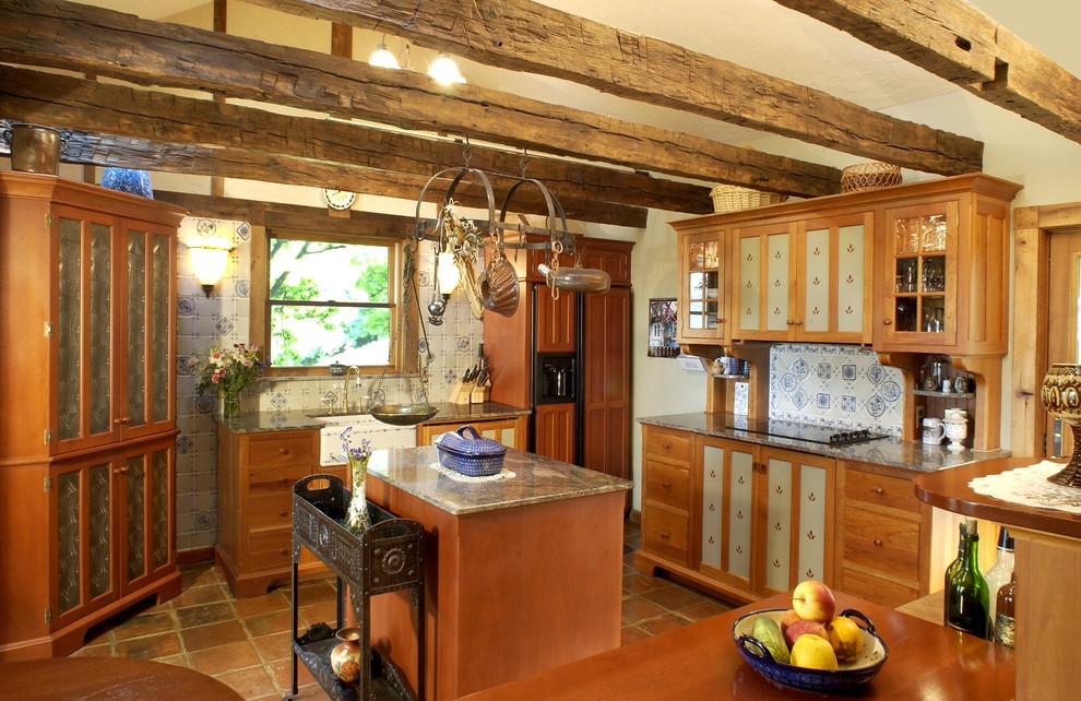 Inredning av ett rustikt kök, med en rustik diskho, släta luckor, skåp i mellenmörkt trä, flerfärgad stänkskydd, integrerade vitvaror, granitbänkskiva och klinkergolv i terrakotta