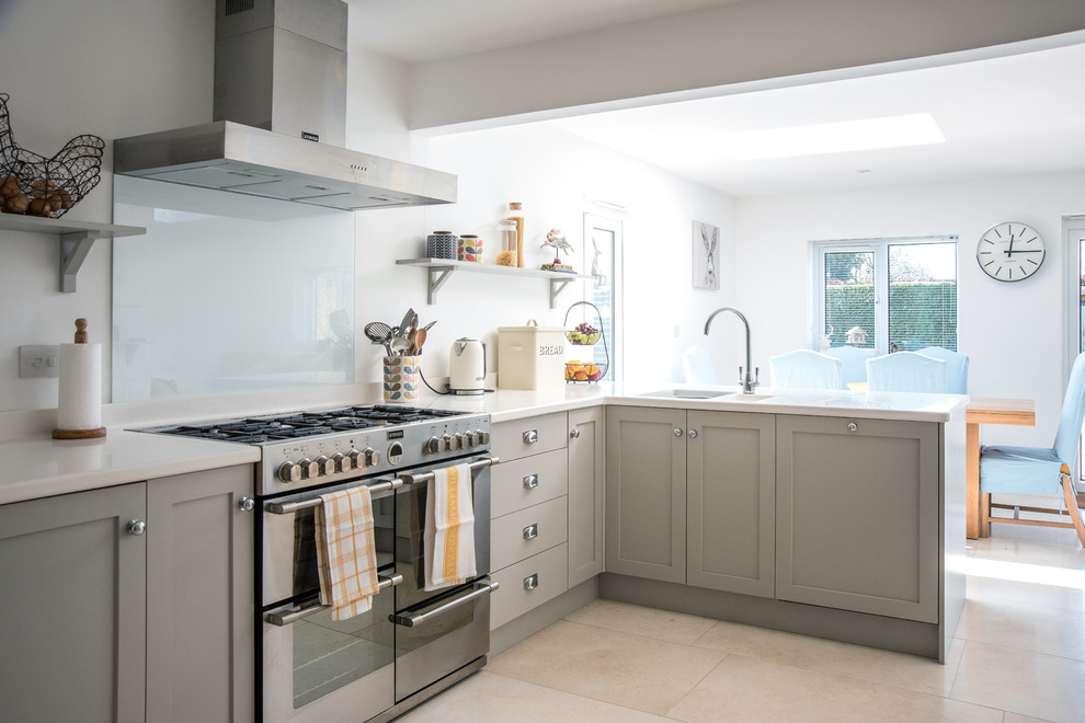 Photo of a medium sized classic l-shaped kitchen/diner in Gloucestershire with an integrated sink, shaker cabinets, grey cabinets, engineered stone countertops, white splashback, glass sheet splashback, stainless steel appliances, travertine flooring, no island, beige floors and white worktops.