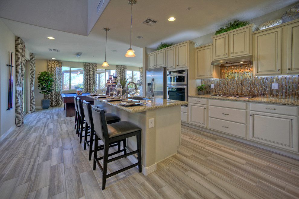 Example of a transitional single-wall ceramic tile open concept kitchen design in Phoenix with a drop-in sink, raised-panel cabinets, white cabinets, granite countertops, metallic backsplash, ceramic backsplash, stainless steel appliances and an island