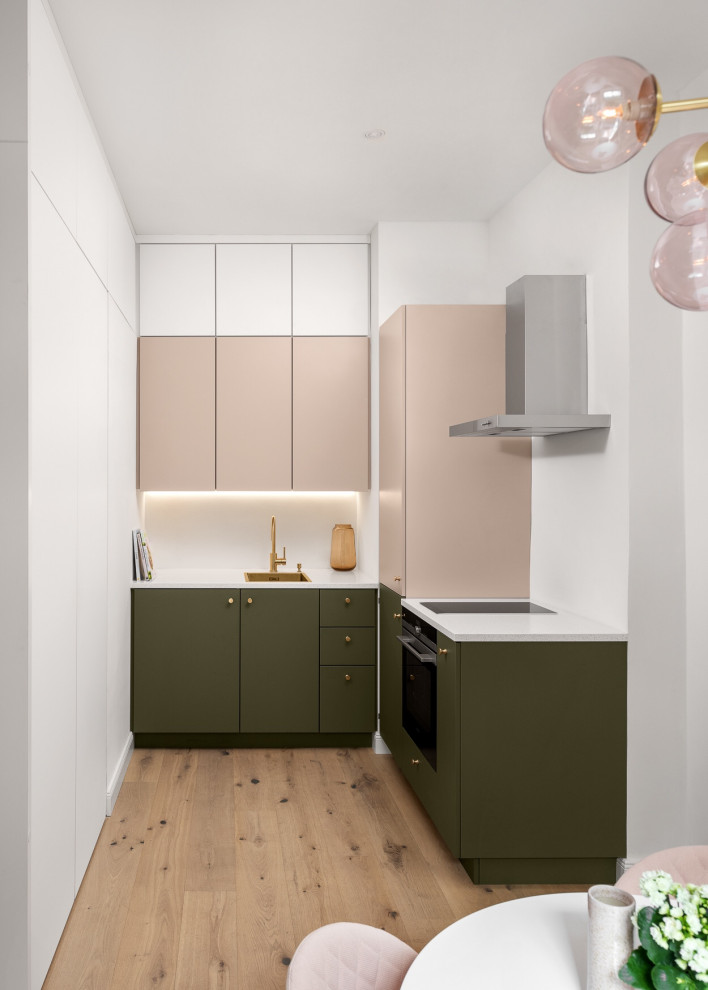 Small trendy l-shaped light wood floor and beige floor open concept kitchen photo in Munich with a single-bowl sink, flat-panel cabinets, green cabinets, solid surface countertops, white backsplash, glass sheet backsplash, black appliances, no island and white countertops