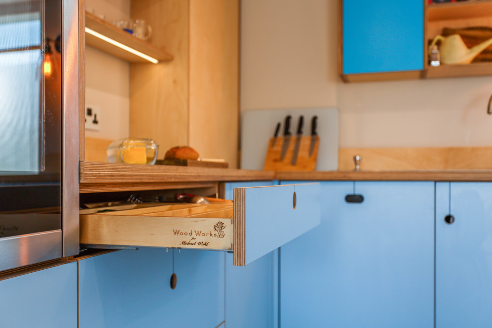 Cette image montre une cuisine américaine bohème en L de taille moyenne avec un placard à porte plane, des portes de placard turquoises, un plan de travail en stratifié, une péninsule et un plan de travail bleu.