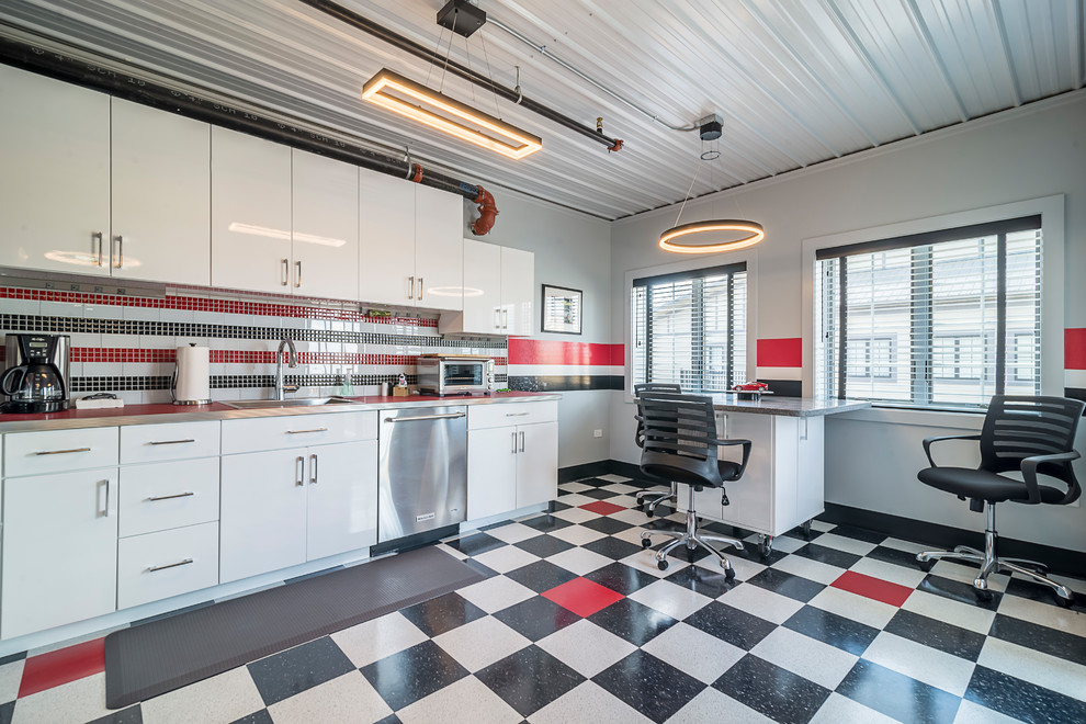 This is an example of a large industrial single-wall kitchen in Chicago with a built-in sink, flat-panel cabinets, white cabinets, stainless steel worktops, multi-coloured splashback, stainless steel appliances, multi-coloured floors, glass tiled splashback and red worktops.