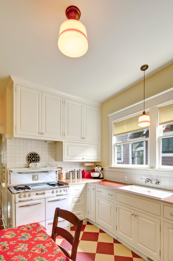 Example of a classic multicolored floor eat-in kitchen design in Portland with a drop-in sink, white appliances, laminate countertops, white cabinets, white backsplash, raised-panel cabinets and red countertops