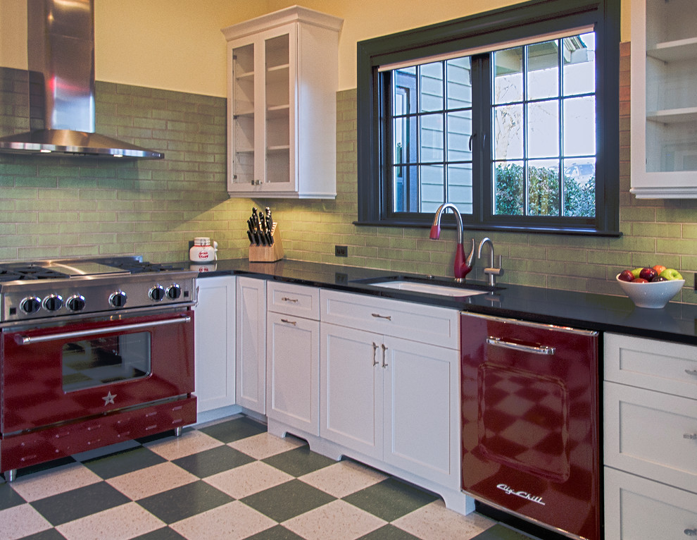 На фото: угловая кухня среднего размера в стиле ретро с обеденным столом, врезной мойкой, фасадами в стиле шейкер, белыми фасадами, зеленым фартуком, цветной техникой, островом и полом из линолеума