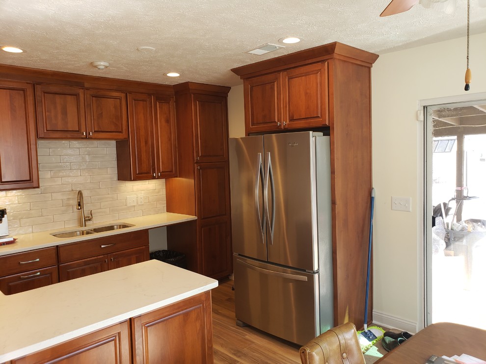 Inredning av ett klassiskt mellanstort vit vitt kök, med en dubbel diskho, luckor med upphöjd panel, skåp i mellenmörkt trä, bänkskiva i kvarts, vitt stänkskydd, stänkskydd i keramik, rostfria vitvaror, klinkergolv i keramik, en halv köksö och brunt golv