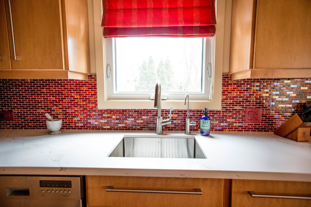 トロントにあるエクレクティックスタイルのおしゃれなキッチン (アンダーカウンターシンク、フラットパネル扉のキャビネット、淡色木目調キャビネット、珪岩カウンター、赤いキッチンパネル、ガラス板のキッチンパネル、シルバーの調理設備、淡色無垢フローリング、茶色い床、白いキッチンカウンター) の写真