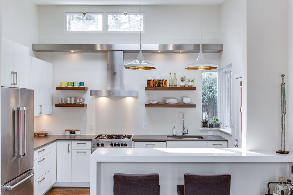 Kleine Moderne Küche mit Unterbauwaschbecken, flächenbündigen Schrankfronten, Küchengeräten aus Edelstahl, braunem Holzboden und Halbinsel in Washington, D.C.