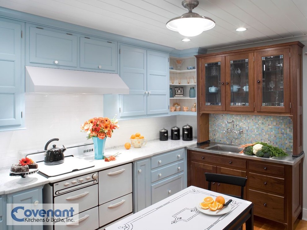 На фото: кухня в стиле кантри с монолитной мойкой, синими фасадами, мраморной столешницей, белым фартуком, фартуком из плитки кабанчик, светлым паркетным полом и белой техникой