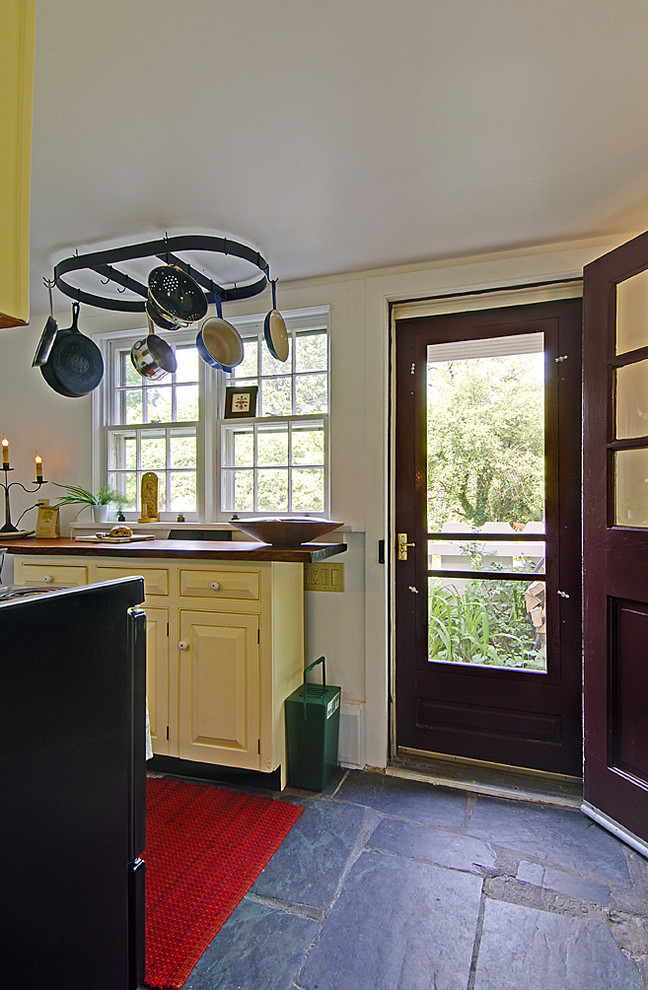 Eklektisk inredning av ett avskilt, litet u-kök, med en rustik diskho, luckor med upphöjd panel, gula skåp, träbänkskiva, vitt stänkskydd, vita vitvaror och skiffergolv