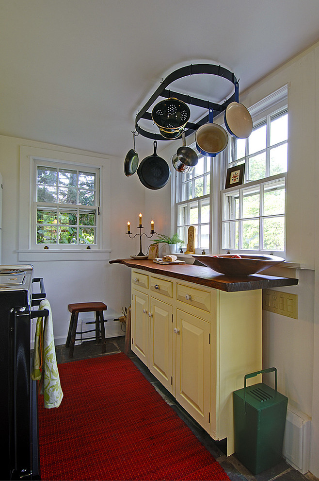 Inredning av ett eklektiskt avskilt, litet u-kök, med en rustik diskho, luckor med upphöjd panel, gula skåp, träbänkskiva, vitt stänkskydd, vita vitvaror och skiffergolv
