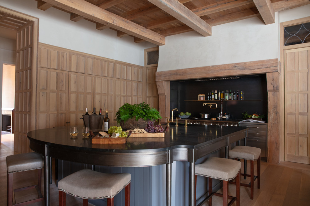 Klassisk inredning av ett avskilt, mellanstort svart svart kök, med luckor med upphöjd panel, skåp i mellenmörkt trä, bänkskiva i täljsten, svart stänkskydd, stänkskydd i metallkakel, rostfria vitvaror, mellanmörkt trägolv, en köksö och beiget golv
