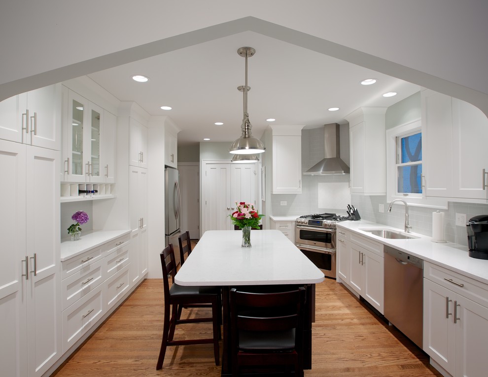 Enclosed kitchen - mid-sized contemporary galley medium tone wood floor and brown floor enclosed kitchen idea in Chicago with an undermount sink, shaker cabinets, white cabinets, solid surface countertops, gray backsplash, porcelain backsplash, stainless steel appliances and an island