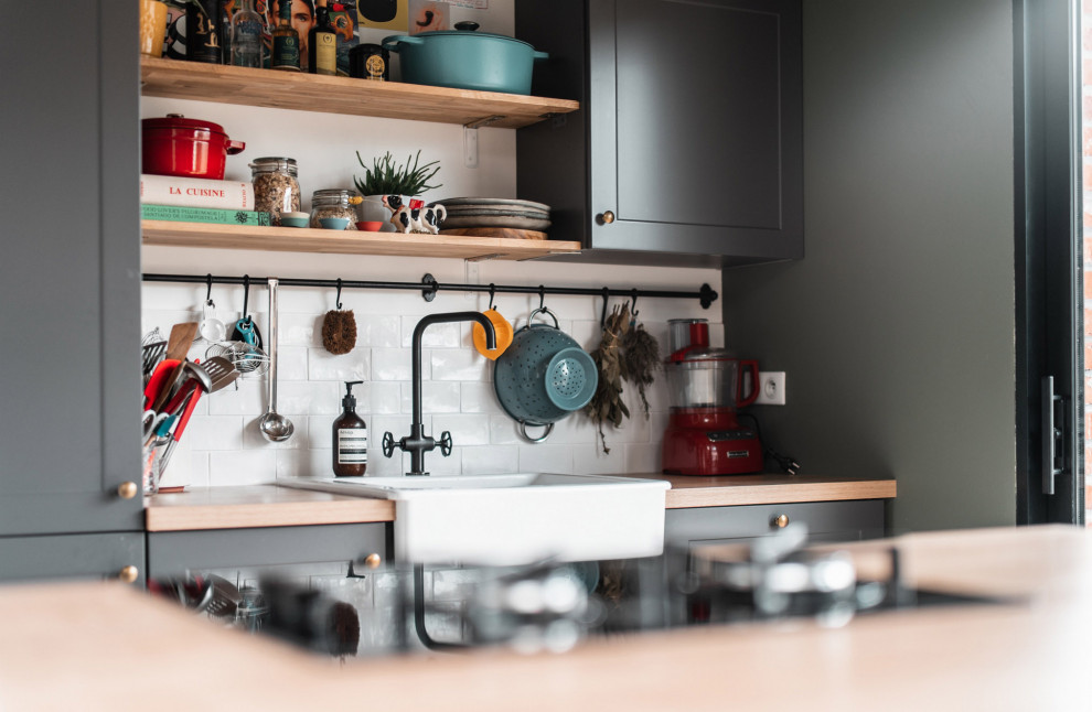 Large contemporary kitchen in Lille with a belfast sink, green cabinets, wood worktops, white splashback, ceramic splashback, black appliances, cement flooring, an island and beige worktops.