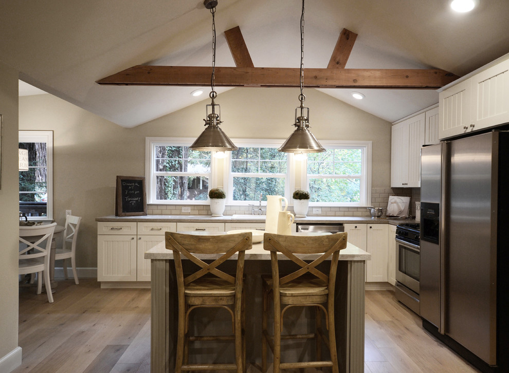 Inspiration for a mid-sized rustic l-shaped medium tone wood floor and brown floor open concept kitchen remodel in Sacramento with a drop-in sink, shaker cabinets, white cabinets, brown backsplash, stone tile backsplash, stainless steel appliances and an island