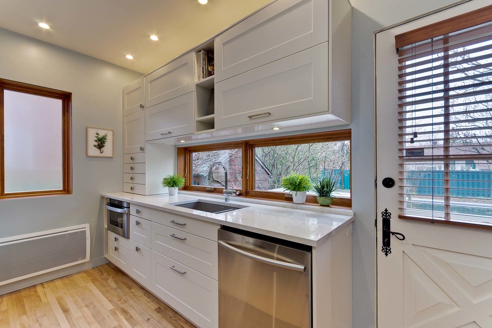 Modern inredning av ett litet kök, med en undermonterad diskho, släta luckor, vita skåp, bänkskiva i koppar, blått stänkskydd, stänkskydd i mosaik, rostfria vitvaror, ljust trägolv och beiget golv