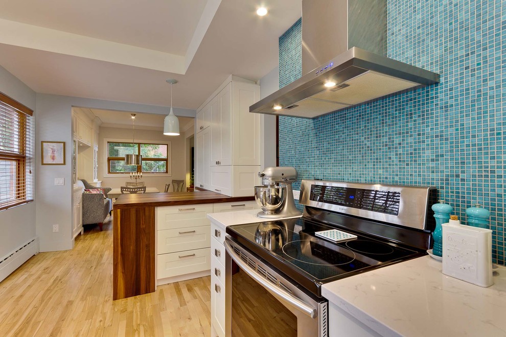 Bild på ett litet eklektiskt kök, med en undermonterad diskho, släta luckor, vita skåp, bänkskiva i koppar, blått stänkskydd, stänkskydd i mosaik, rostfria vitvaror, ljust trägolv och beiget golv