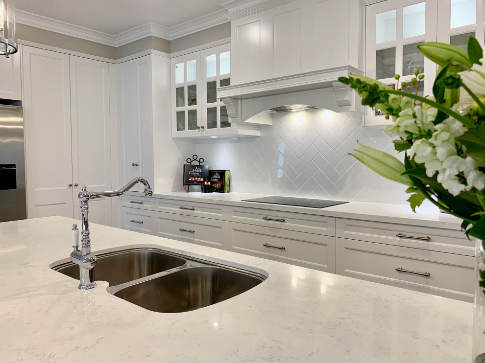 Exempel på ett mycket stort klassiskt vit vitt kök, med en undermonterad diskho, luckor med infälld panel, grå skåp, bänkskiva i kvarts, vitt stänkskydd, stänkskydd i sten, svarta vitvaror, mellanmörkt trägolv, en köksö och brunt golv