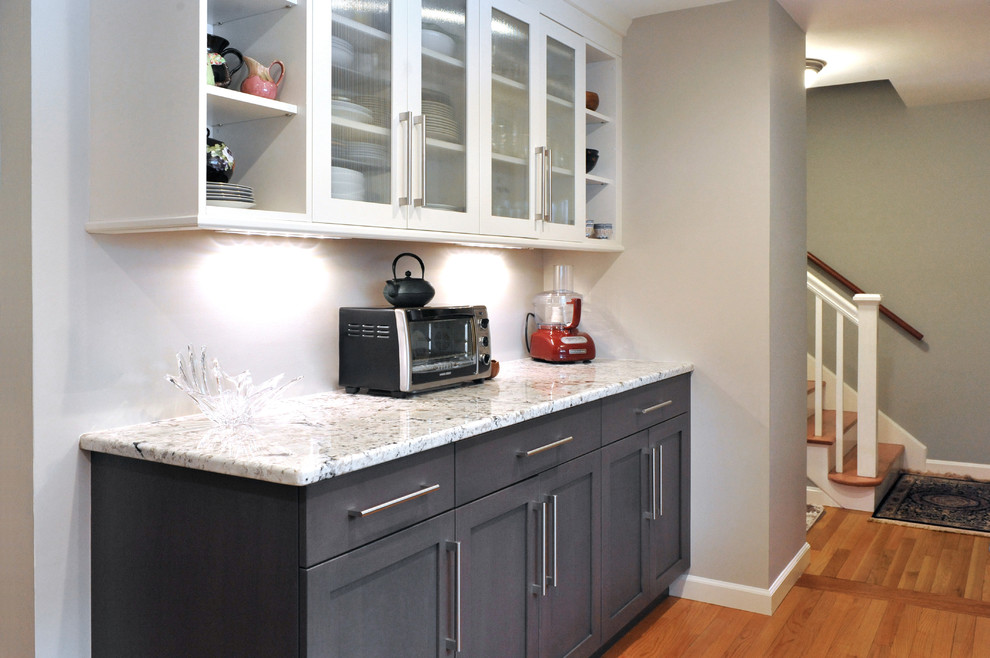 Bild på ett mellanstort, avskilt funkis u-kök, med en enkel diskho, släta luckor, vita skåp, granitbänkskiva, grått stänkskydd, rostfria vitvaror och ljust trägolv