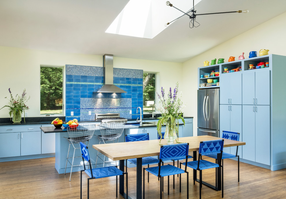 This is an example of a contemporary l-shaped kitchen/diner in Other with a submerged sink, flat-panel cabinets, blue cabinets, blue splashback, stainless steel appliances, medium hardwood flooring, an island, brown floors and black worktops.