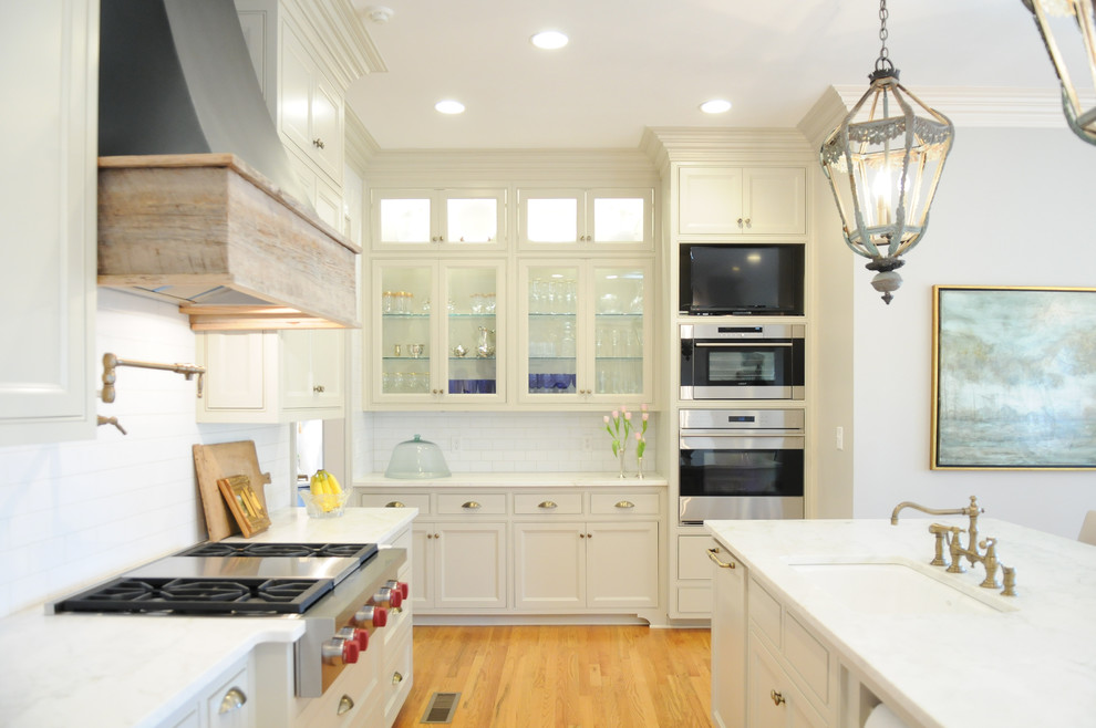 Example of a transitional light wood floor kitchen pantry design in Birmingham with a farmhouse sink, flat-panel cabinets, beige cabinets, marble countertops, white backsplash, subway tile backsplash, paneled appliances and an island