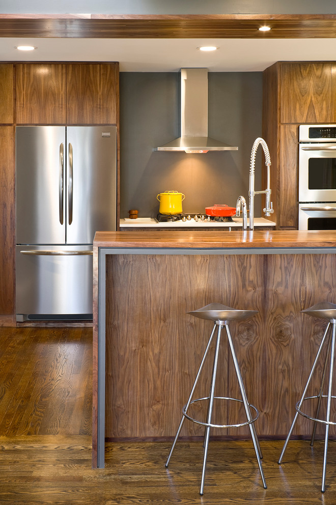 Idée de décoration pour une cuisine design en U et bois brun de taille moyenne avec un placard à porte plane, un plan de travail en bois et un électroménager en acier inoxydable.