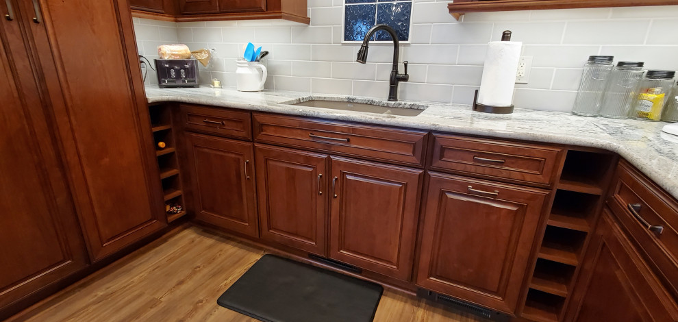 Photo of a medium sized traditional u-shaped enclosed kitchen in Other with a submerged sink, raised-panel cabinets, medium wood cabinets, granite worktops, grey splashback, metro tiled splashback, vinyl flooring, an island, brown floors and white worktops.