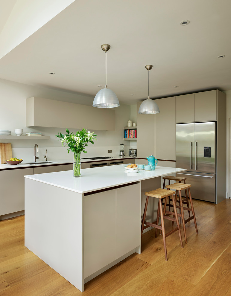 Large contemporary l-shaped kitchen/diner in London with flat-panel cabinets, beige cabinets, composite countertops, medium hardwood flooring, an island, beige floors and white worktops.