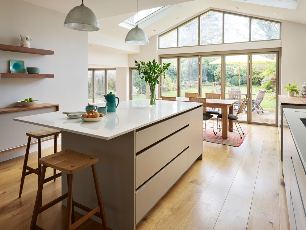 Foto di una grande cucina minimal con ante lisce, ante beige, top in superficie solida, pavimento in legno massello medio, pavimento beige e top bianco